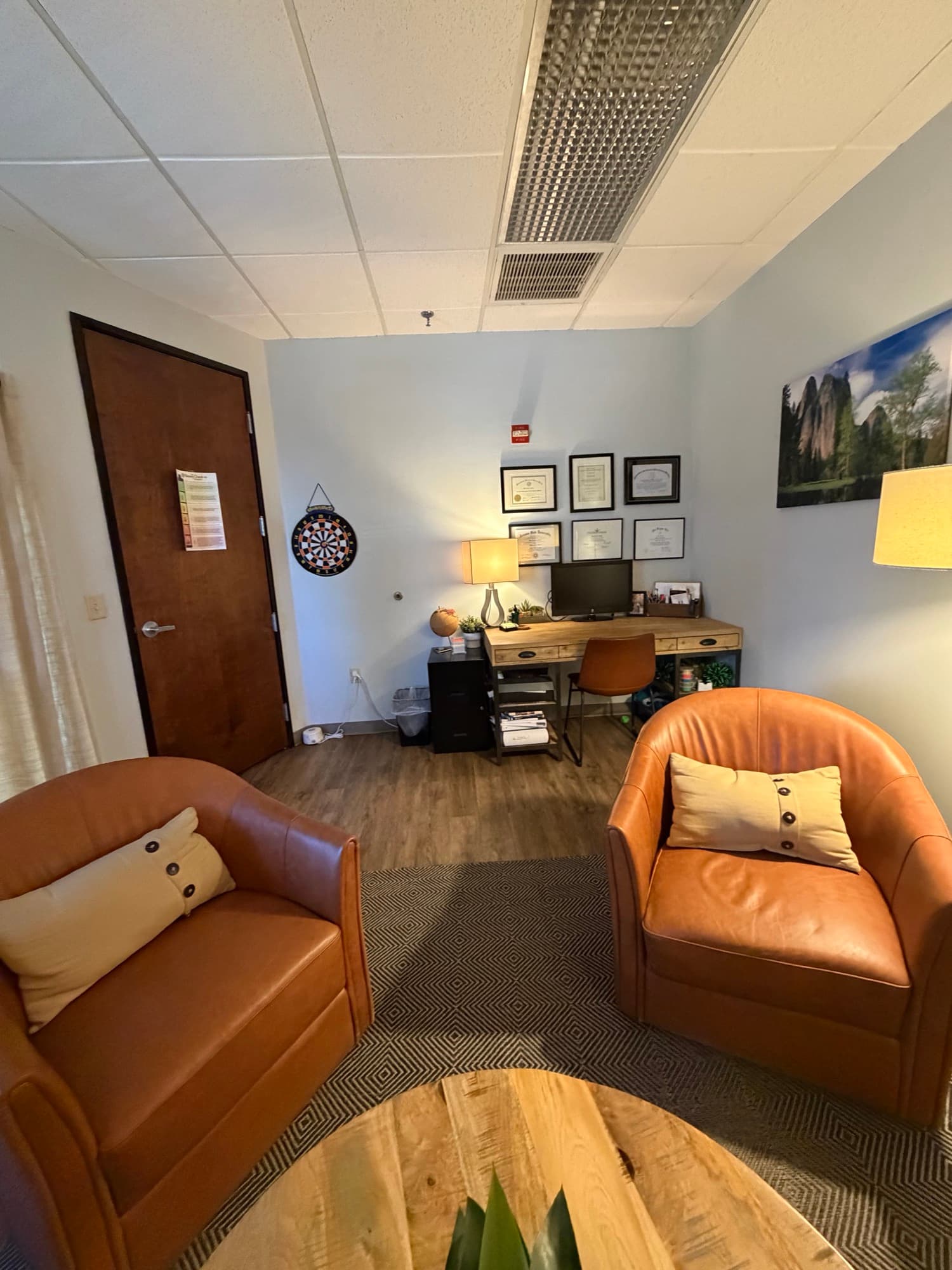 Therapy office with leather chairs, a desk, and a dartboard